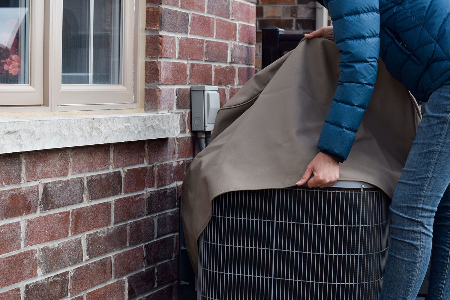 woman putting a cover on air conditioner unit outside of house
